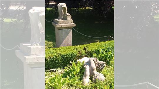 Eine Sandsteinfigur liegt schwer beschädigt in einem Garten.