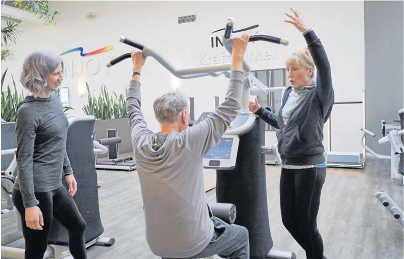Krebspatientin: Das Training gibt mir etwas Halt „Und noch einmal, kräftig.“ Elke Paschek (r.) mit Eberhard Kleuker, erkrankt an einem Tumor im Rachenraum, im Braunschweiger Injoy-Fitnessstudio. Kurs-Trainerin Jana Cordes (li.) beobachtet beide bei der Übung am sogenannten „Latzug“, der große Muskelpartien am Rücken trainiert. Foto: Stefan Lohmann/Regios24