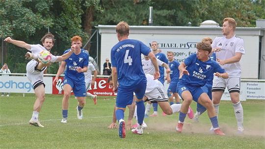 Fußballspieler in blauen und weißen Trikots kämpfen um den Ball auf einem Spielfeld vor einer Zuschauertribüne mit Werbebannern