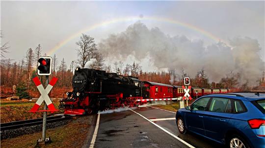 Die Harzer Schmalspurbahn fährt über einen Bahnübergang, im Hintergrund ein Regenbogen.