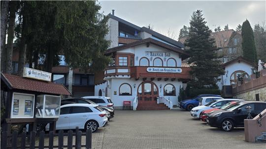 Gasthaus mit traditioneller Architektur, mehreren geparkten Autos davor und einem Schild.