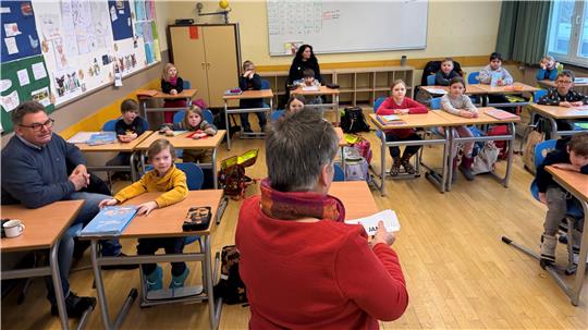 Das Foto zeigt einen Klassenraum mit Grundschüler an dem Bürgermeister links.