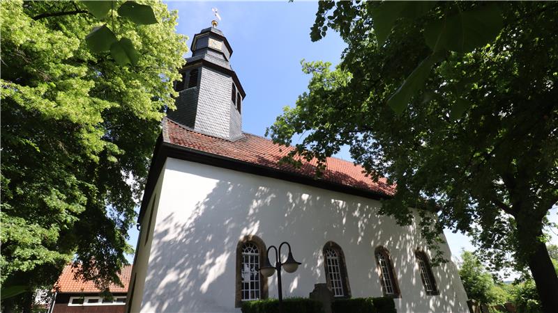 Kirche vor blauen Himmel, von mächtigen Bäumen umgeben.