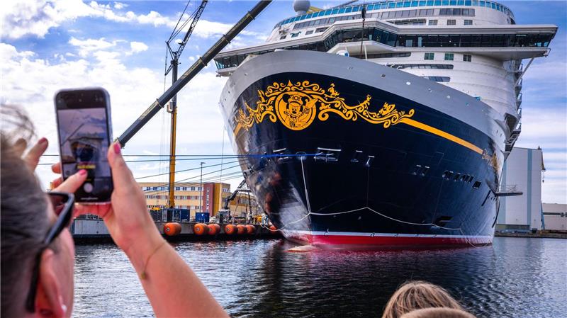 Urlauber fotografieren bei einer Hafenrundfahrt das neue Kreuzfahrtschiff „Disney Adventure“ am Ausrüstungskai der Wismarer Werft.