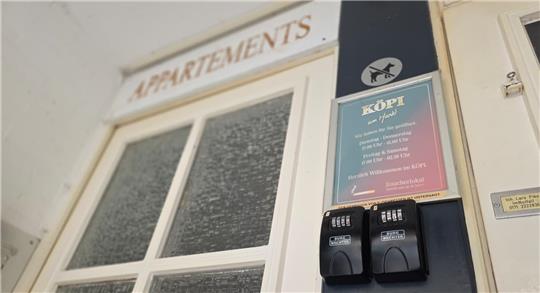 Eingangstür mit Milchglasscheiben und Schild mit der Aufschrift 'APPARTEMENTS' sowie zwei schwarze Schlüsselsafes an der Wand
