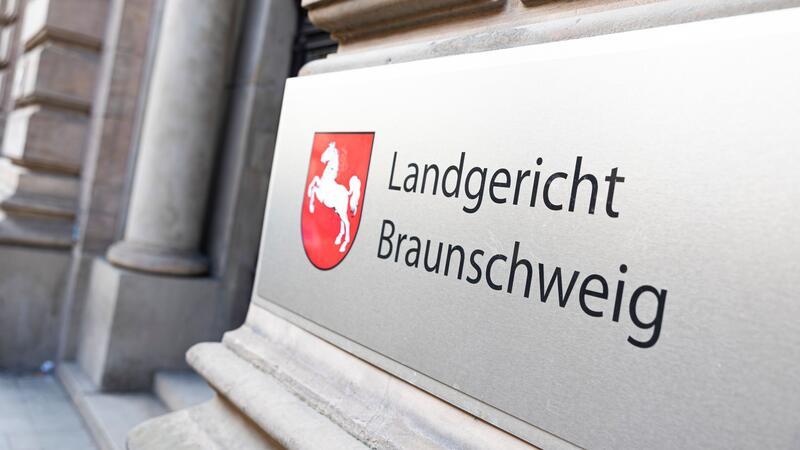 Nahaufnahme eines steinernen Schilds mit rotem Wappen und der Aufschrift 'Landgericht Braunschweig' an einem historischen Gebäude