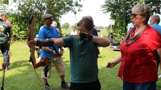 Ute Koch (rechts) gibt dem elfjährigen Aaron Tipps für den richtigen Umgang mit einem Jagdbogen. Auch Georg Koch (Hintergrund, blaues Shirt) steht als Ansprechpartner für interessierte Bogenschützen parat.