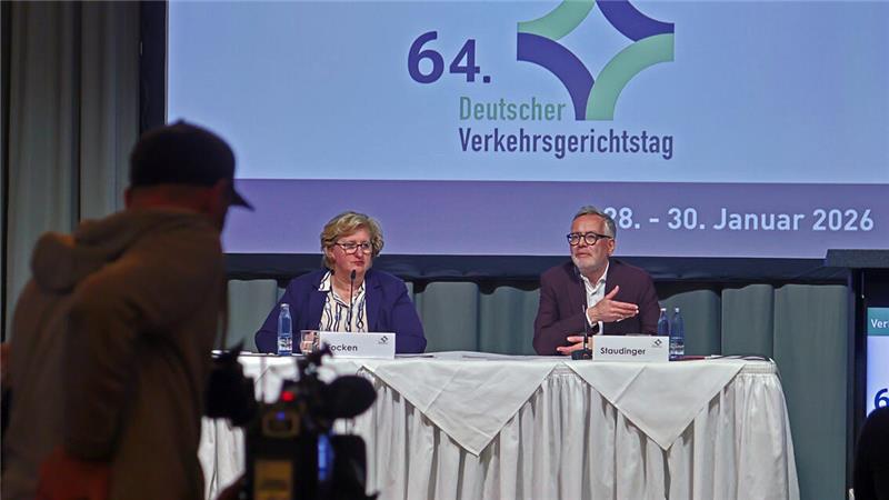 Zwei Personen sitzen an einem mit weißem Tuch bedeckten Tisch vor einer Leinwand mit dem Schriftzug '64. Deutscher Verkehrsgerichtstag 28. - 30. Januar 2026'