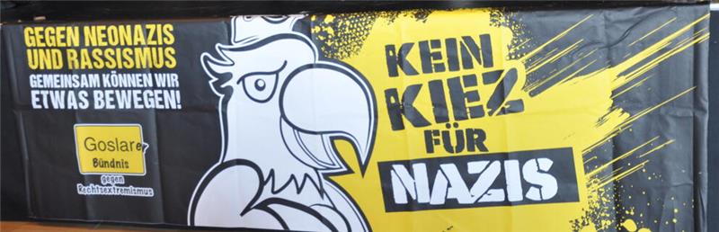 Krieg der Infos: Podcaster erklären Goslar die Fake-News-Welt Transparent mit einer stilisierten Adlerillustration und dem Text 'Gegen Neonazis und Rassismus gemeinsam können wir etwas bewegen! Kein Kiez für Nazis' in schwarz-gelber Gestaltung