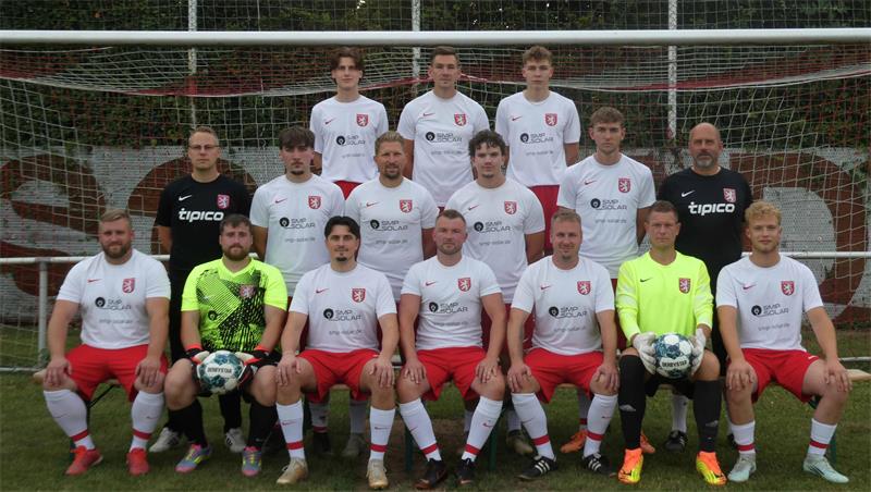 Fußballmannschaft mit 12 Spielern und zwei Torhütern in weißen Trikots und roten Hosen vor einem Tor auf dem Spielfeld