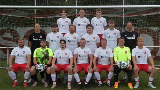 Fußballmannschaft mit 12 Spielern und zwei Torhütern in weißen Trikots und roten Hosen vor einem Tor auf dem Spielfeld
