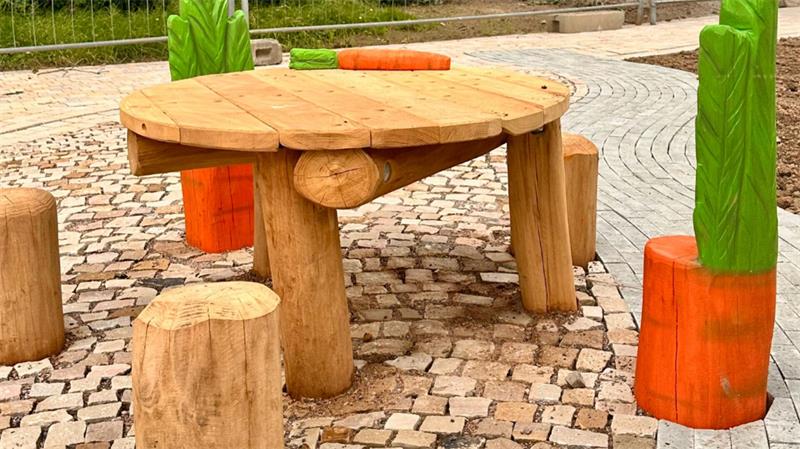 Seesener Züchner-Spielplatz wird später fertig als geplant Runder Holztisch mit drei Baumstammhockern auf gepflastertem Boden und bunten, pflanzenförmigen Dekorationen