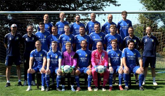 Fußballmannschaft in blauen Trikots und zwei Torhüter in pinken Trikots posieren vor einem Fußballtor auf einem Rasenplatz