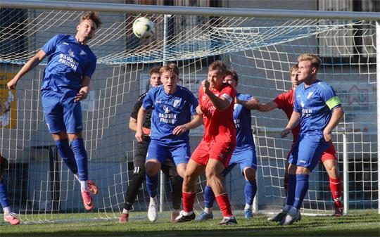 Fußballspieler in blauen und roten Trikots springen und kämpfen vor dem Tor um den Ball