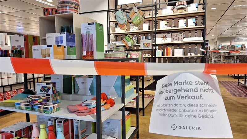 Ein rot-weißes Absperrband hängt vor einem Tisch mit Geschirr in einer Galeria-Filiale. An dem Band hängt eine Notiz: „Diese Marke steht vorübergehend nicht zum Verkauf.“