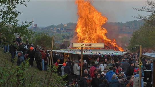 Große Menschenmenge vor einem großen, lodernden Feuer in einer offenen Landschaft.