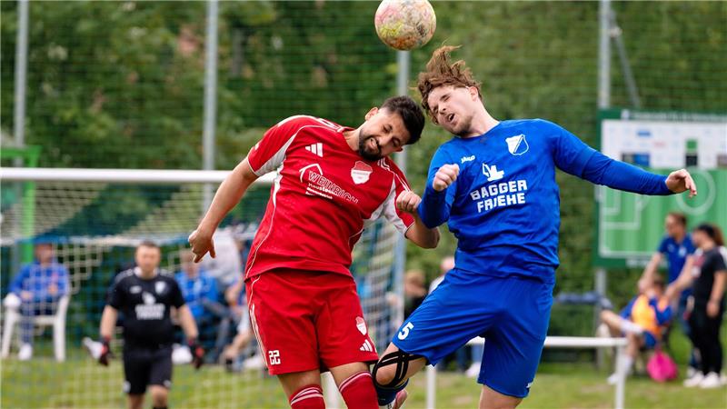 Zwei Fußballspieler in Rot und Blau springen zum Kopfball vor einem Tor mit Torwart im Hintergrund
