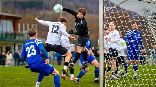 Fußballspieler springen im Strafraum vor dem Tor um den Ball, der Torwart in schwarzer Kleidung hebt die Hand, um den Ball abzuwehren.