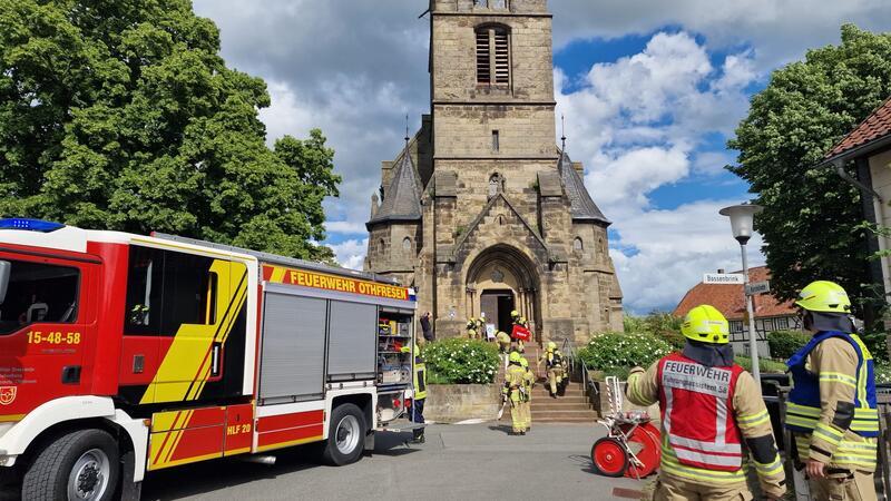 Feuerwehrleute in Schutzkleidung vor einer historischen Kirche mit einem Feuerwehrfahrzeug auf der Straße