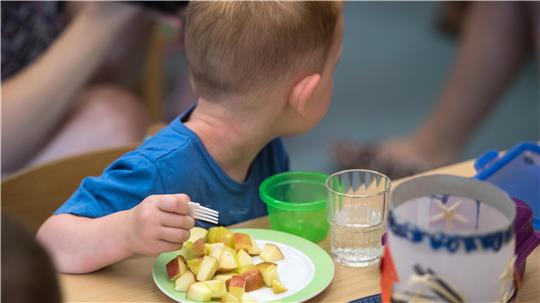 Ein Kindergartenkind isst einen aufgeschnittenen Apfel.
