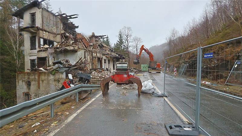 Das Foto zeigt einen Blick auf die Bundesstraße 498 im Okertal. Links ist die Ruine der "Villa Helene" zu sehen, auf der gesperrten Straße trägt ein Bagger die Trümmer des Gebäudes ab.