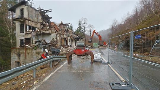 Das Foto zeigt einen Blick auf die Bundesstraße 498 im Okertal. Links ist die Ruine der "Villa Helene" zu sehen, auf der gesperrten Straße trägt ein Bagger die Trümmer des Gebäudes ab.