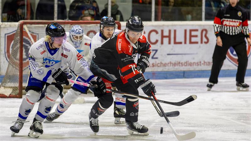 Eishockeyspieler in schwarzer und weißer Ausrüstung kämpfen um den Puck vor dem Tor, im Hintergrund Schiedsrichter und Torwart