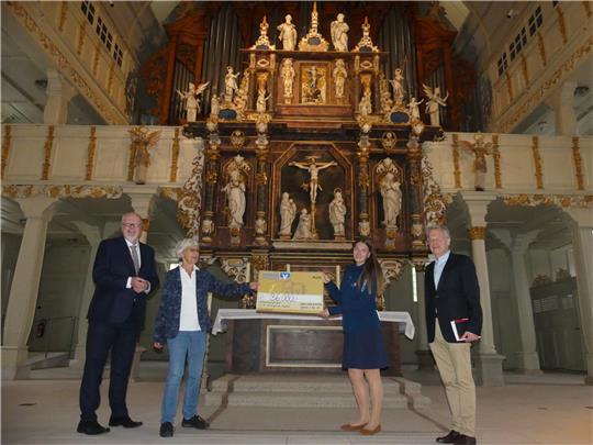 Volksbank-Vorstand Torsten Janßen, Dorothee Austen, Clarissa Evans und Hansjochen Schwieger (v. li.) bei der symbolischen Scheckübergabe. Die VR-Stiftung und die Volksbank haben die Sanierung des Altars mit 36.000 Euro unterstützt. Foto: Römhild