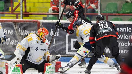 Eishockeyszene vor dem Tor mit Torwart in weißer Ausrüstung und mehreren Spielern in schwarzen und weißen Trikots im Zweikampf um den Puck.
