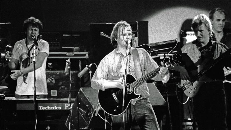 Schwarz-weiß-Foto einer Band mit mehreren Musikern, von denen einer eine Gitarre spielt und singt