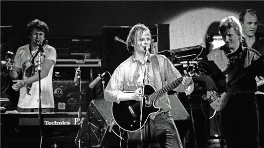Schwarz-weiß-Foto einer Band mit mehreren Musikern, von denen einer eine Gitarre spielt und singt