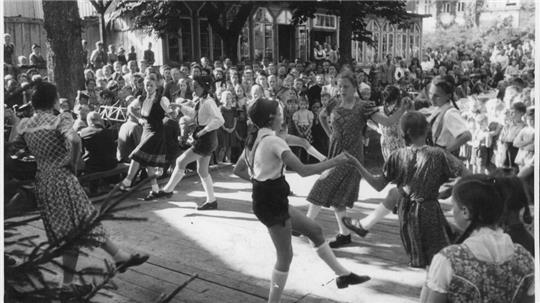 Volle Straßen, lebendige Bergstadt: Bei einer Pressefahrt durch den Harz in Altenau 1950 unterhält die Harzklub-Jugend die Gäste mit Tanzdarbietungen. Altenau will an vergangene Zeiten anknüpfen.