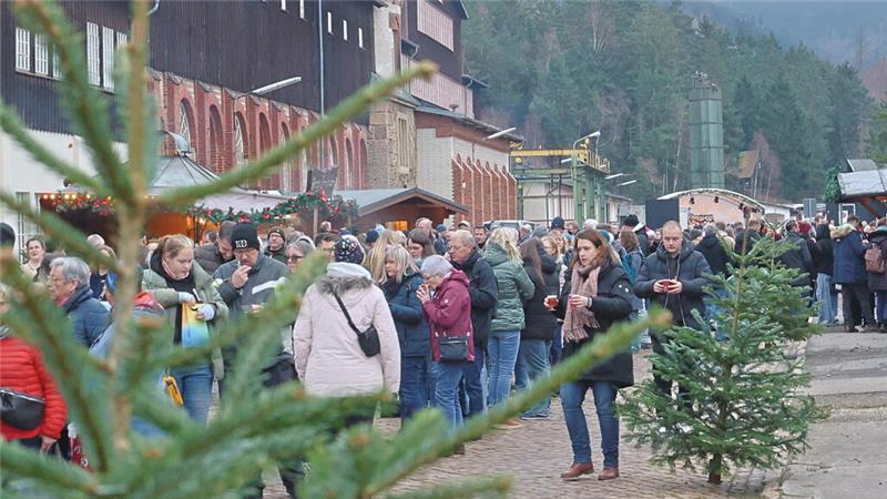 Viele Menschen gehen mit Glühweintassen in der Hand über eine gepflasterte und mit Weihnachtsbäumen geschmückte Straße. 