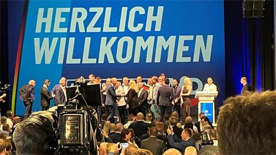 Viele Menschen auf einer Bühne, dahinter der Schriftzug: Herzlich willkommen.