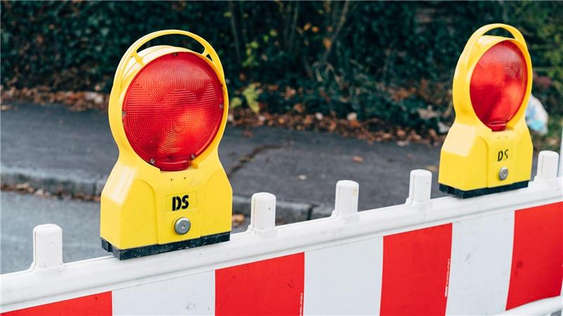 Gelb-rote Warnleuchten auf weiß-roter Absperrung vor unscharfem Hintergrund mit Laub