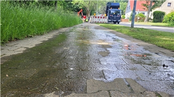 Ein nasser Gehweg, im Hintergrund eine Baustelle.