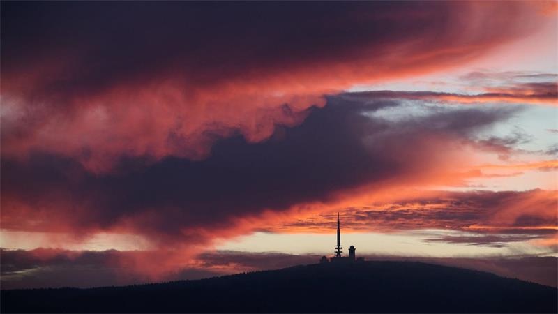 Vom Sonnenaufgang rötlich verfärbt zeigt sich der Himmel über dem Brocken in Sachsen-Anhalt.