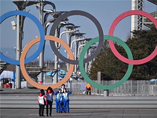 Von Olympia-Stimmung ist in Peking wenig zu spüren: Volunteers stehen vor den olympischen Ringen für ein Selfie. Foto: Peter Kneffel/dpa
