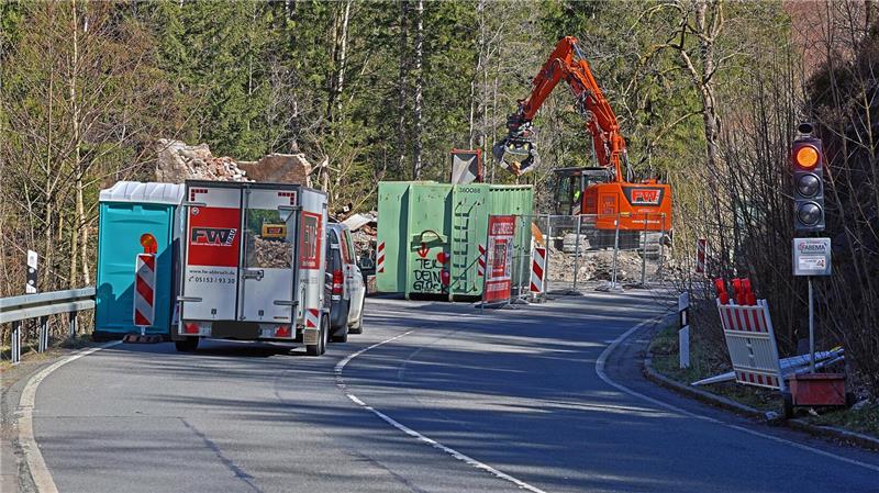 Baustelle auf einer Landstraße mit Absperrungen, einem Baustellenfahrzeug, einem mobilen Toilettenhäuschen und einem Bagger, der Material bewegt