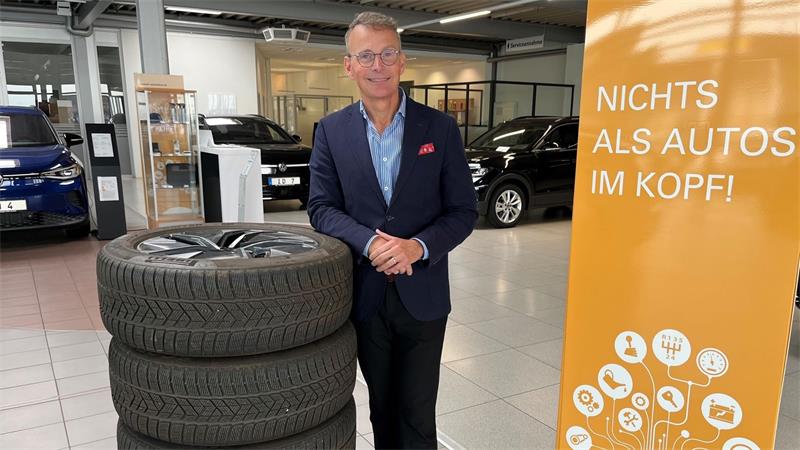 Ein Mann steht in der Halle eines Autohauses und blickt freundlich in die Kamera.