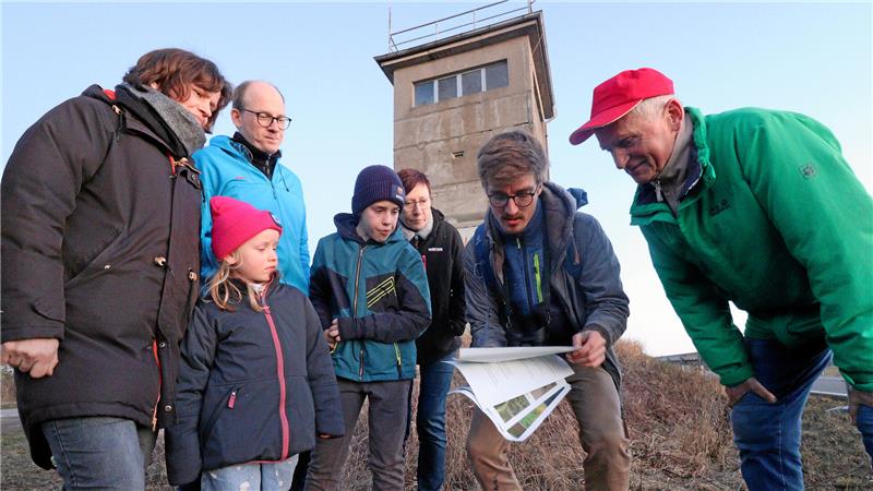 Menschen blicken in Aufzeichnungen, im Hintergrund ein alter DDR-Grenzzaun.