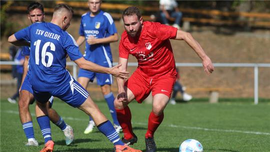 Fußballspieler in blauer und roter Spielkleidung kämpfen um den Ball auf einem Spielfeld mit Ballustrade im Hintergrund