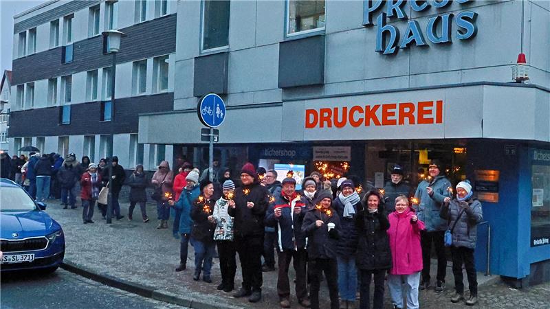 Der GZ-Schweinchenverkauf läuft in Goslar auf Hochtouren Gruppe von Menschen steht mit Kerzen vor einem Gebäude mit dem Schriftzug 'DRUCKEREI' und 'Pressehaus'