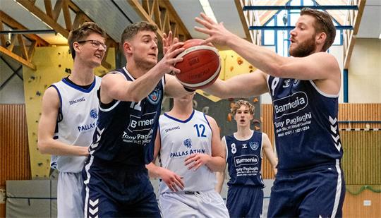 Fünf Basketballspieler in Aktion in einer Halle, drei in dunkelblauen Trikots und zwei in weißen Trikots, einer hält den Ball