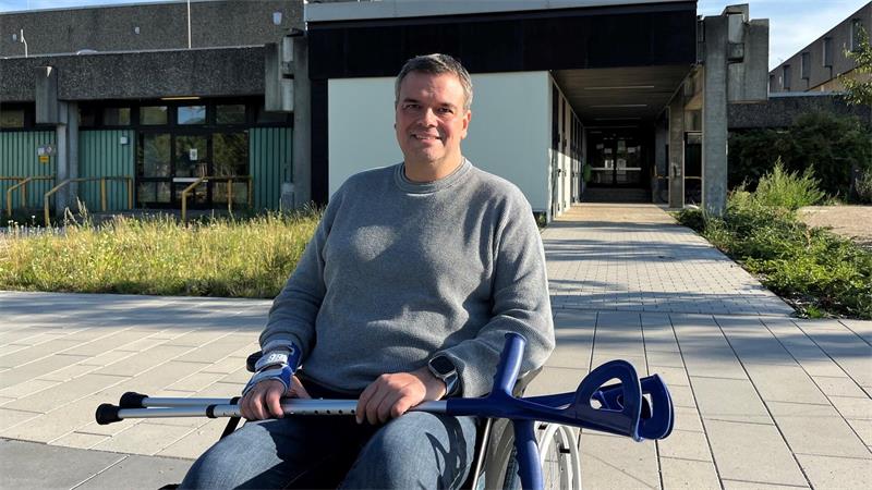 Ein Mann sitzt in einem Rollstuhl, über seinen Beinen liegen Krückstöcke.