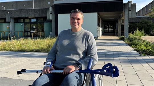 Ein Mann sitzt in einem Rollstuhl, über seinen Beinen liegen Krückstöcke.