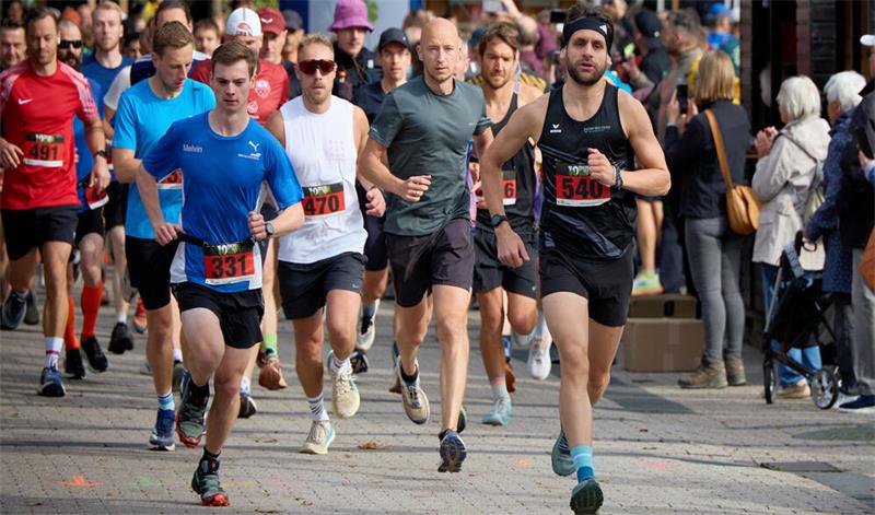 Läufergruppe mit Startnummern läuft auf gepflastertem Weg bei einem Marathon mit Zuschauern am Rand
