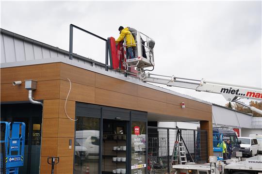 „WE“: Das Schild über dem neuen Haupteingang wird montiert. Im Gebäude untergebracht sind auch eine Bäckereifiliale und eine Poststelle. Foto: Bode