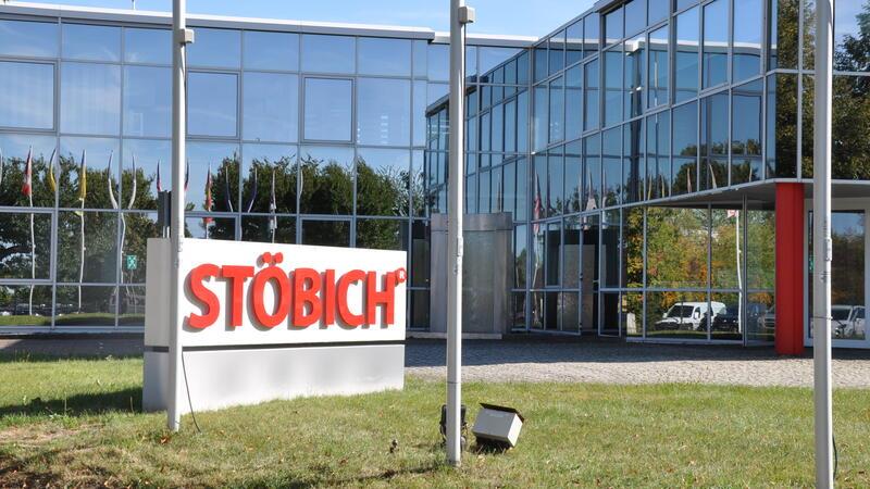 Firmengebäude mit Glasfassade und einem Schild mit der Aufschrift 'STÖBICH' auf einer Wiese davor