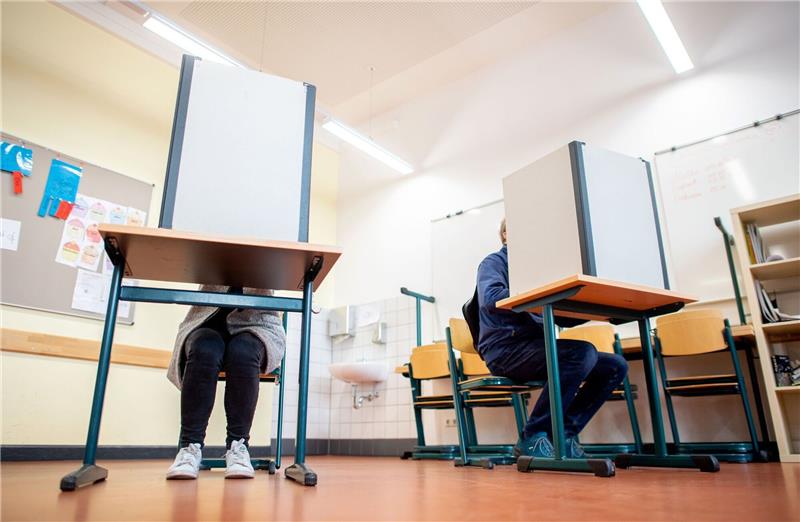 Wähler sitzen in einem Wahlraum in der Lutherschule hinter einem Sichtschutz.